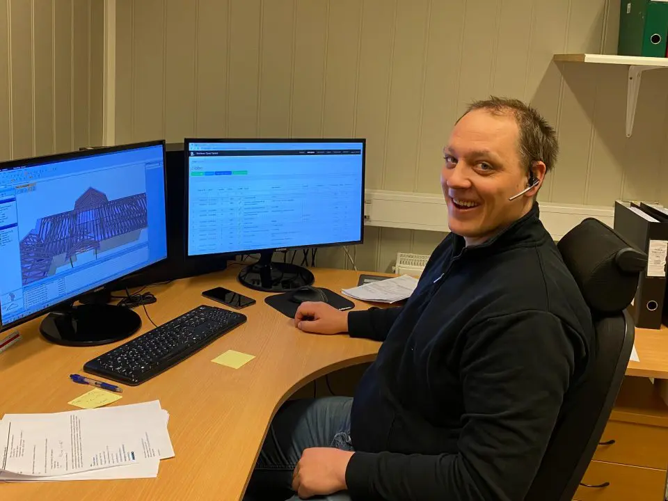 bildet viser en mann som sitter foran to dataskjermer på kontoret og smiler